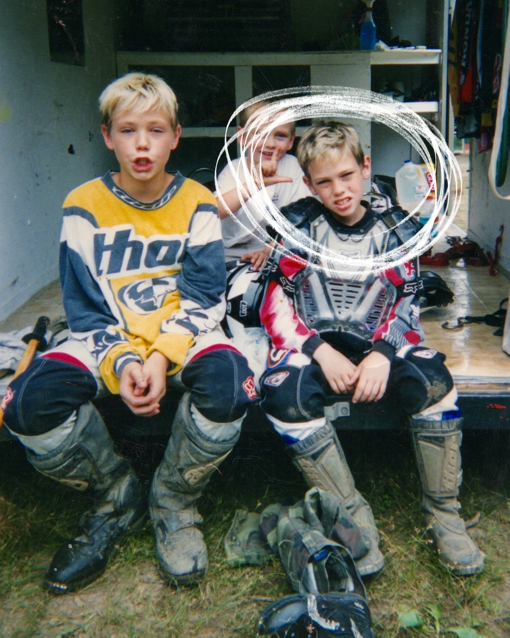 Two boys in motocross gear sitting on the back of a trailer, one circled in white